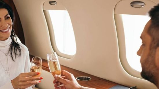 A well-dressed couple clinking champagne glasses while seated next to each other on a private jet.