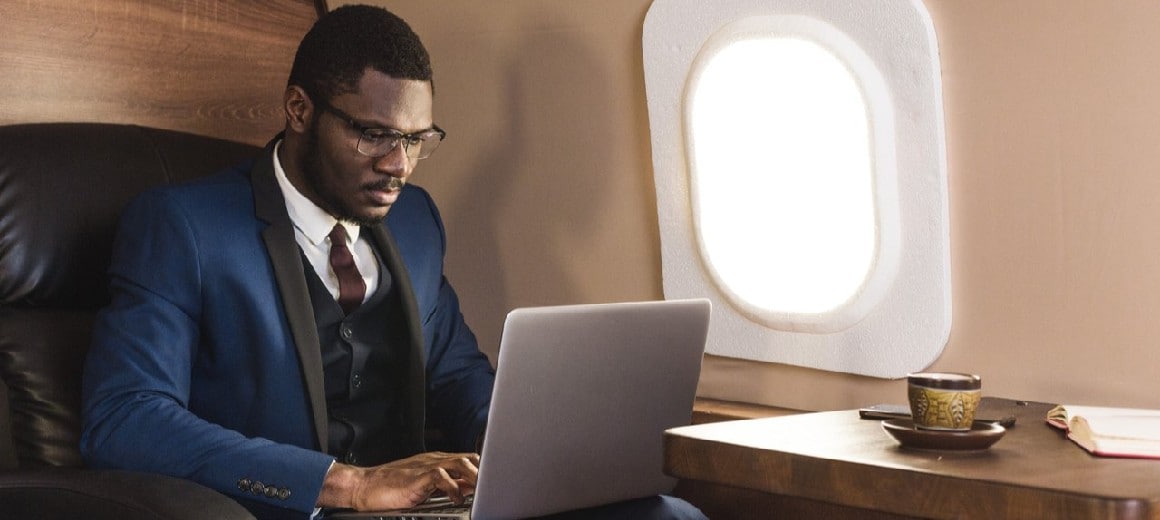 Man working on laptop while sitting in black leather seat on private jet