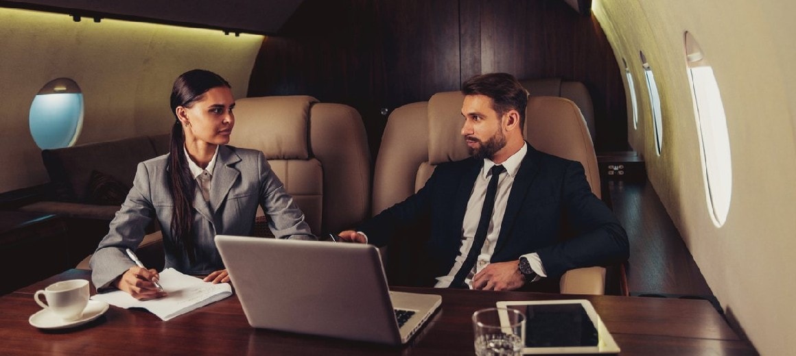 Man and woman doing business in front of a laptop onboard a private jet