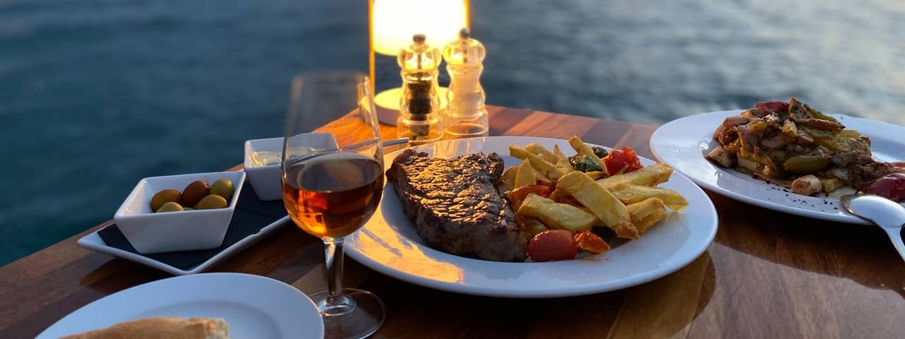 A dinner table set next to the water of a bay at sunset.