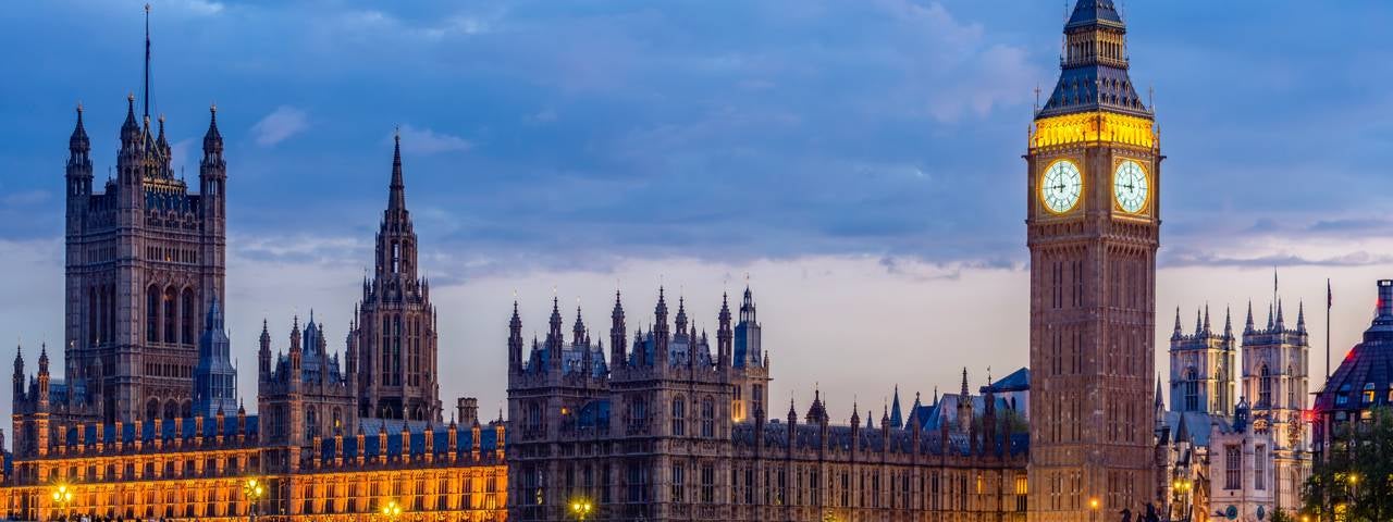 The Houses of Parliament with Big Ben tower and Westminster Bridge at sunset.