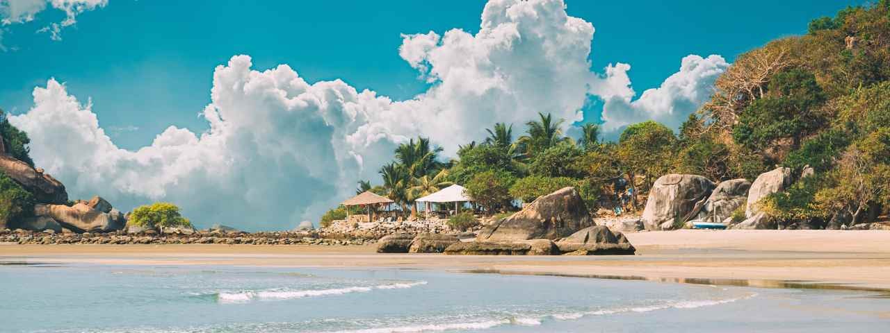 A beautiful beach in Goa with palm trees and some bungalows.