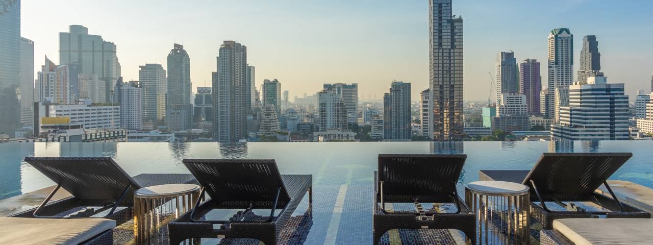Loungers next to a rooftop swimming pool with a view across Bangkok.