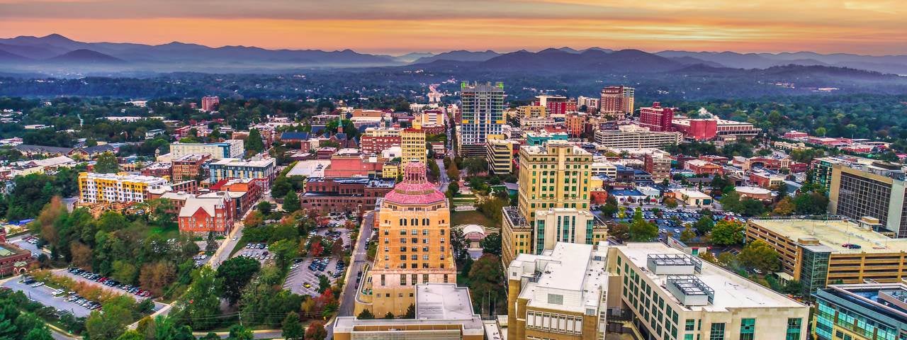 An aerial view of downtown Asheville with the sunset and mountains in the background