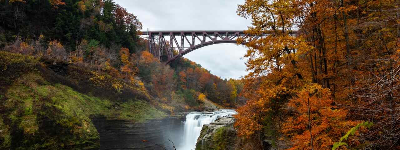 A picturesque bridge crossing a river with trees in autumn colors on each side in the Finger Lakes