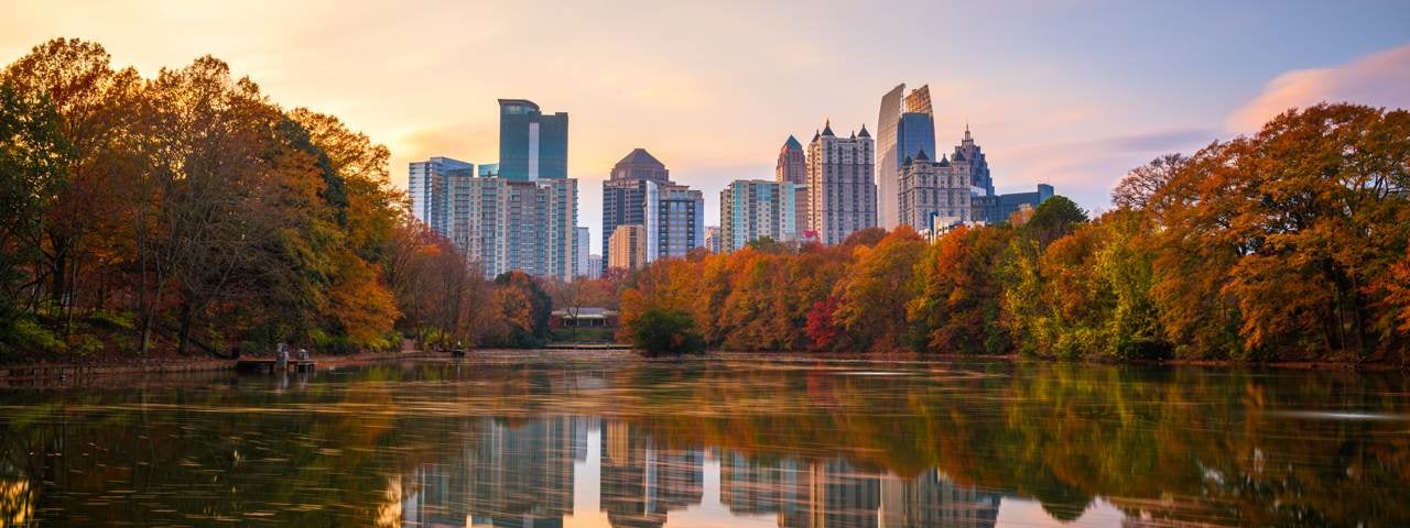 Buildings of Atlanta during a fall sunset with trees and a pond in the foreground.