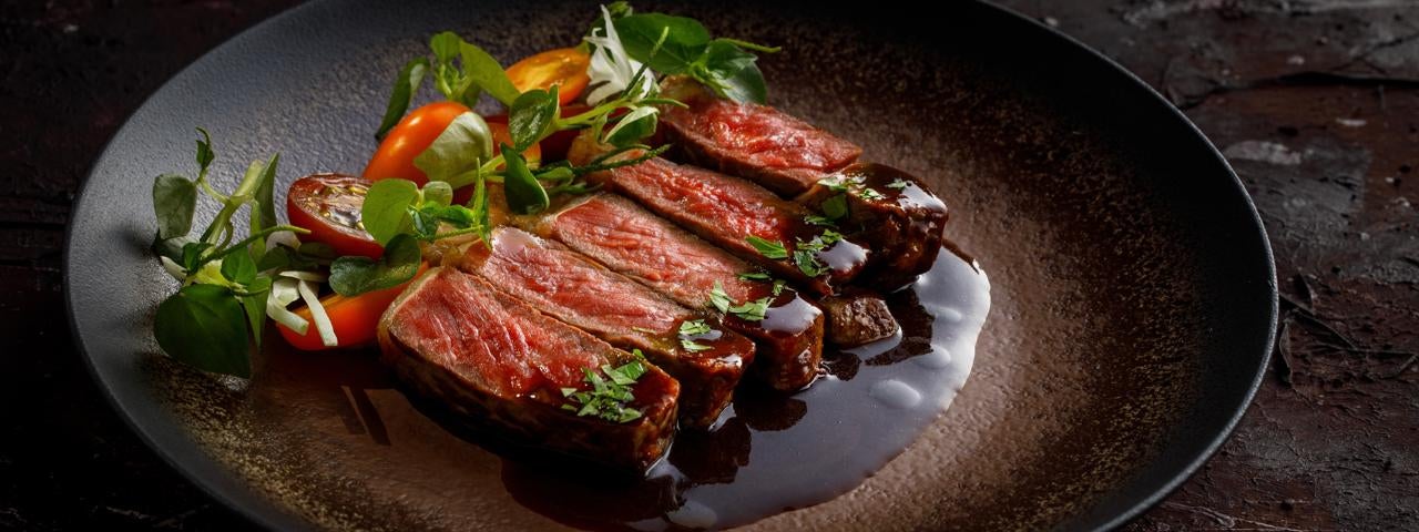 A plate of Australian striploin wagyu beef served with sauce and fresh vegetables.