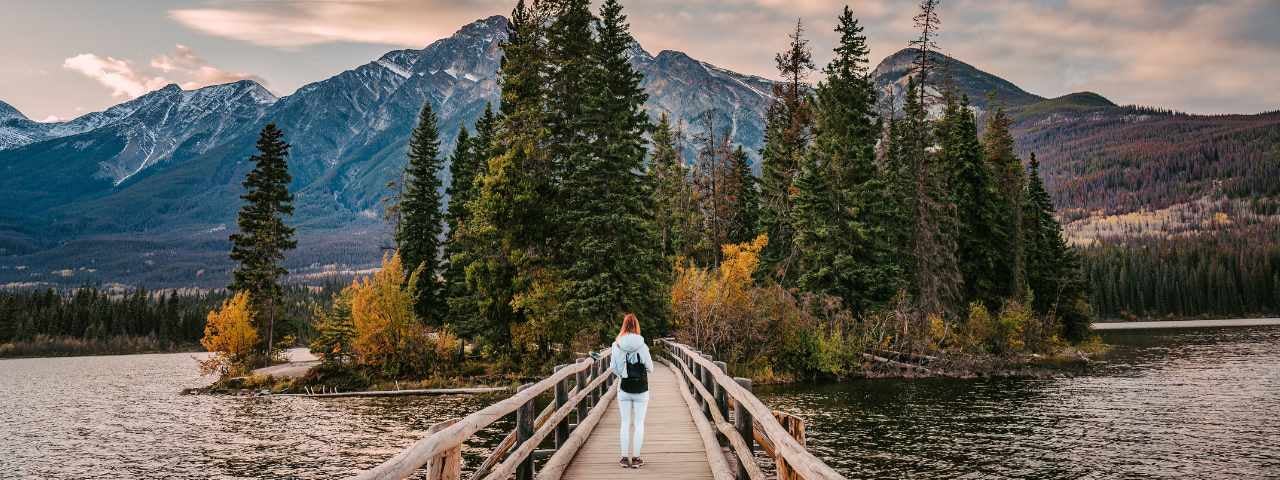 Female tourist standing on a wooden bridge and going to a tiny island on Pyramid Lake in the evening at Jasper National Park, AB, Canada.