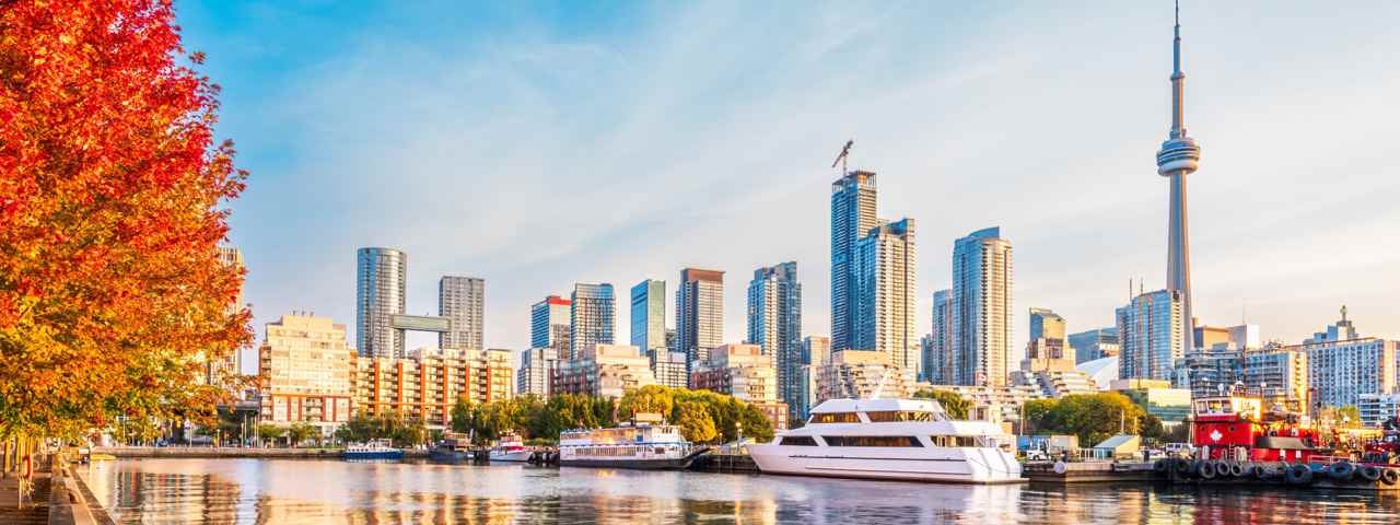 A view of Toronto from the water, with a boat in the foreground and trees in Fall colors.
