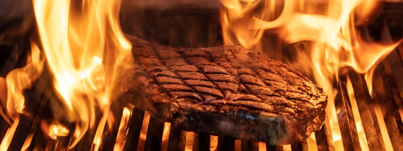 A T-Bone steak being flame grilled.