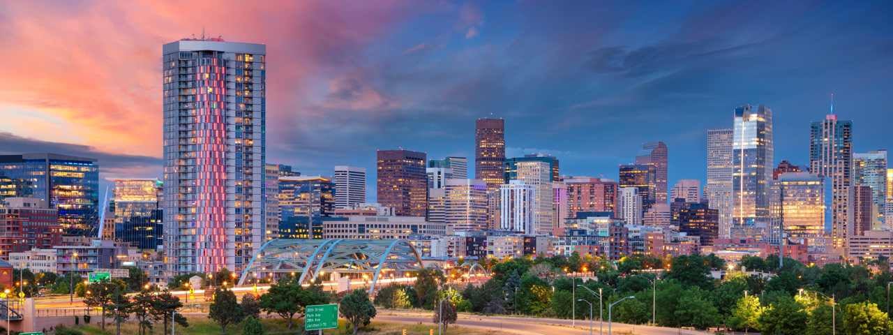 The Denver skyline lit up in the evening with the sunset sky behind it.