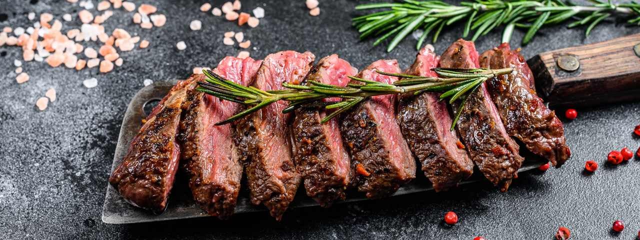 A gourmet steak sliced and lined out on a knife with rosemary, salt, and pepper