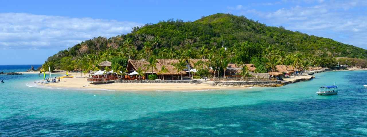 Front view of a thatch resort on the Mamanuca Islands with the ocean and a boat in the foreground.