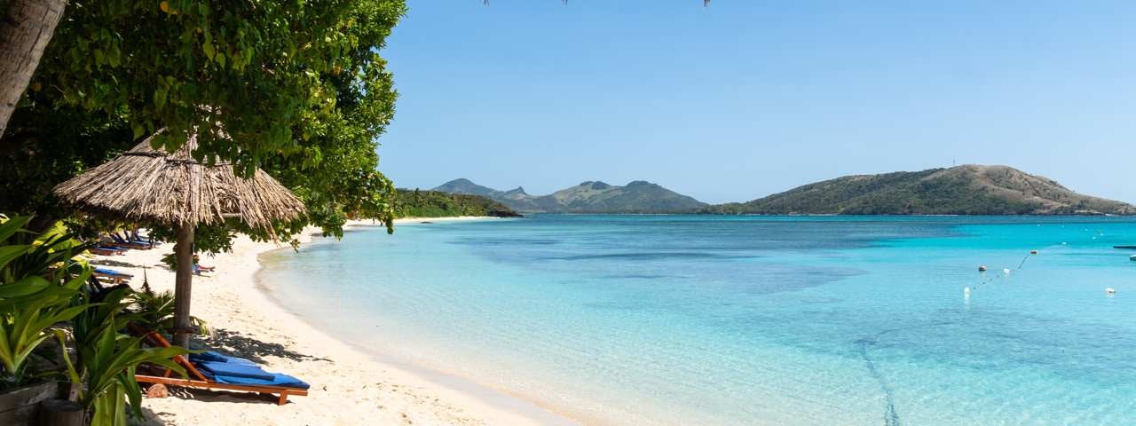 A beach with a thatch umbrella and lounger on the Yasawa Islands in Fiji.