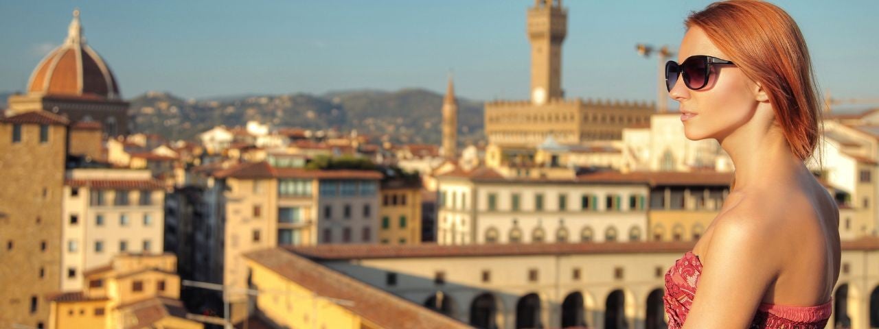 A beautiful woman standing on a balcony in Florence, Italy, overlooking the stunning architecture in the city below. 
