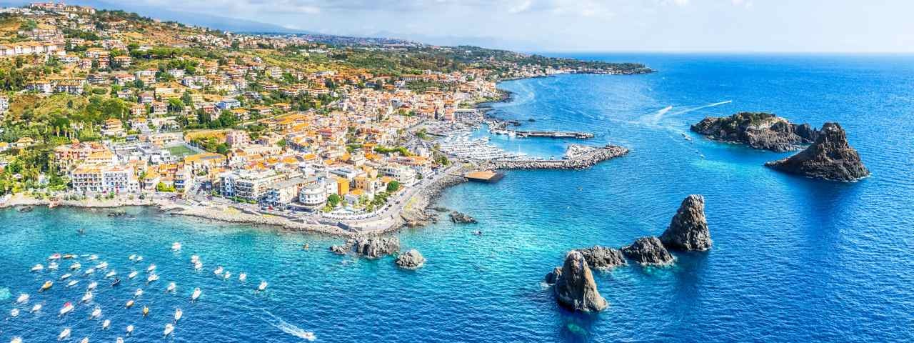 An aerial view of a town in Sicily overlooking the ocean and boats parked in the harbor