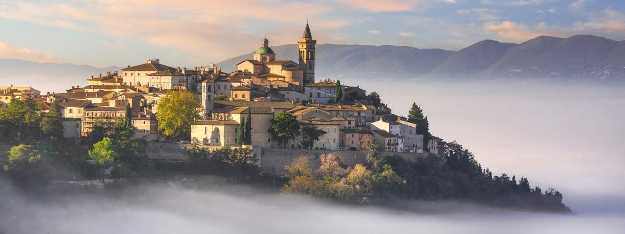 A hilltop town in Umbria surrounded by mist in the morning light.
