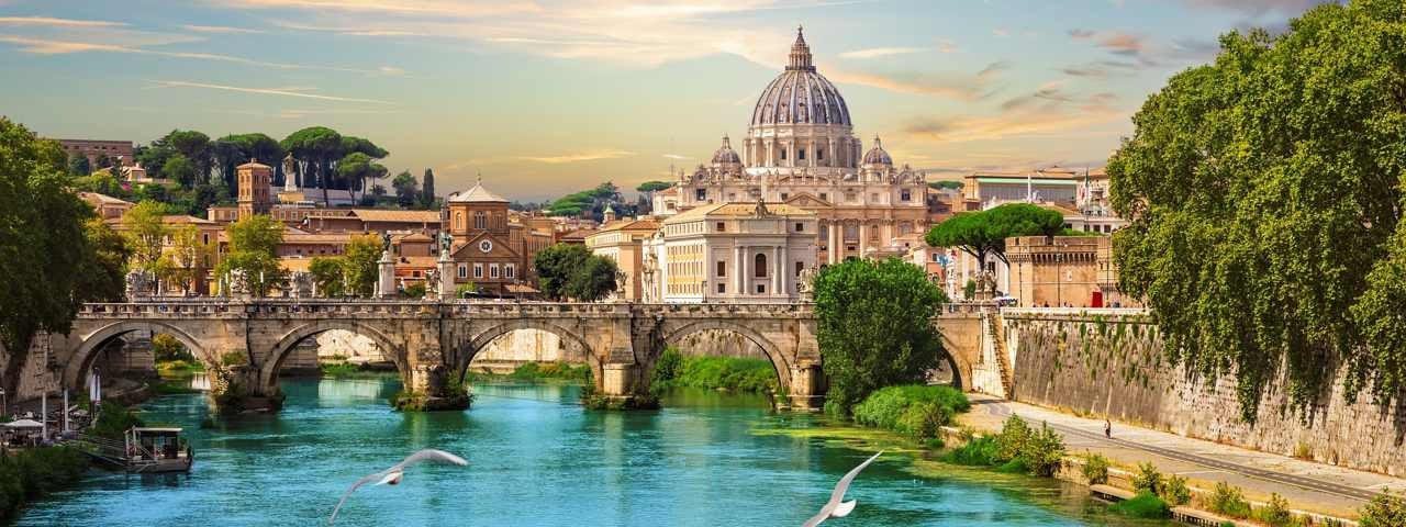 St. Peter’s Basilica in Rome overlooking a bridge and river, with seagulls soaring in the foreground.