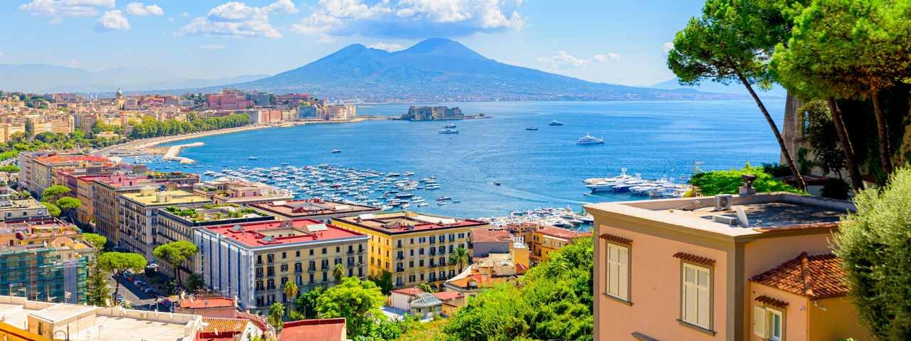 A breathtaking aerial view of a seaside town in Naples, with the ocean in front and Mount Vesuvius towering in the background.
