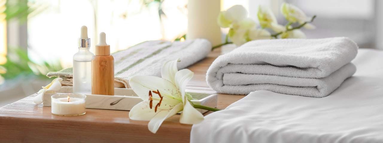 A spa set up with towels, oils, a massage bed and flowers