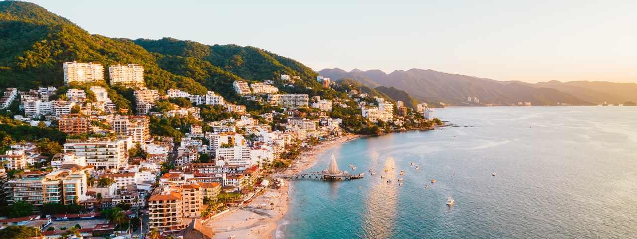 Sunset on a beach with buildings and mountains behind it in Puerto Vallarta.