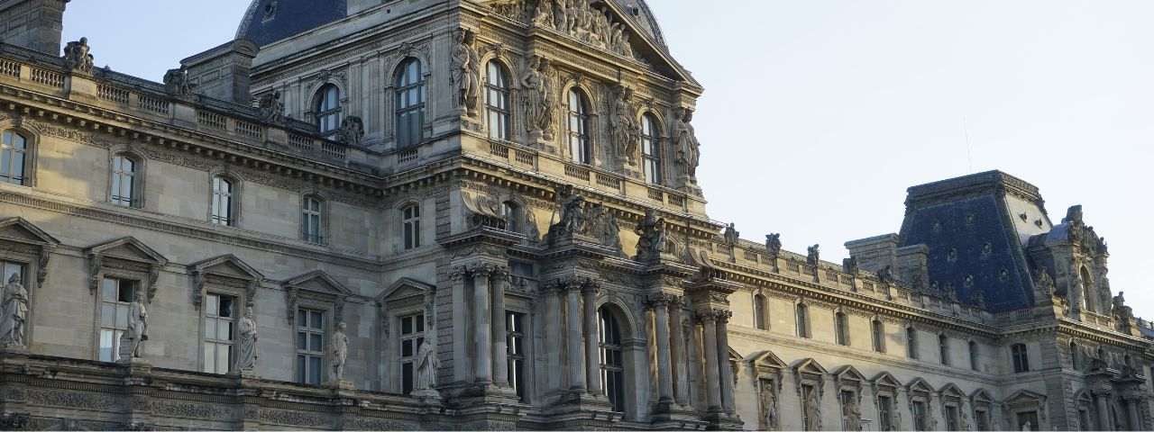 Close-up view of the ornate facade of the Louvre Museum in Paris, France, showcasing classical sculptures, arched windows, and detailed stonework under a clear sky.