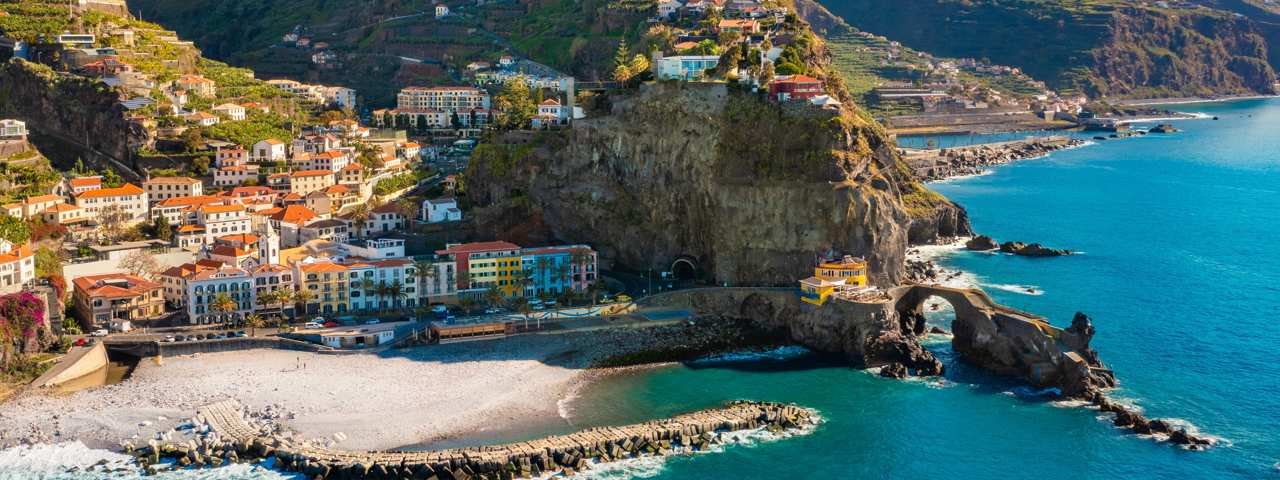 A picturesque bridge crossing a river in the Duora Valley surrounded by a village and mountains.