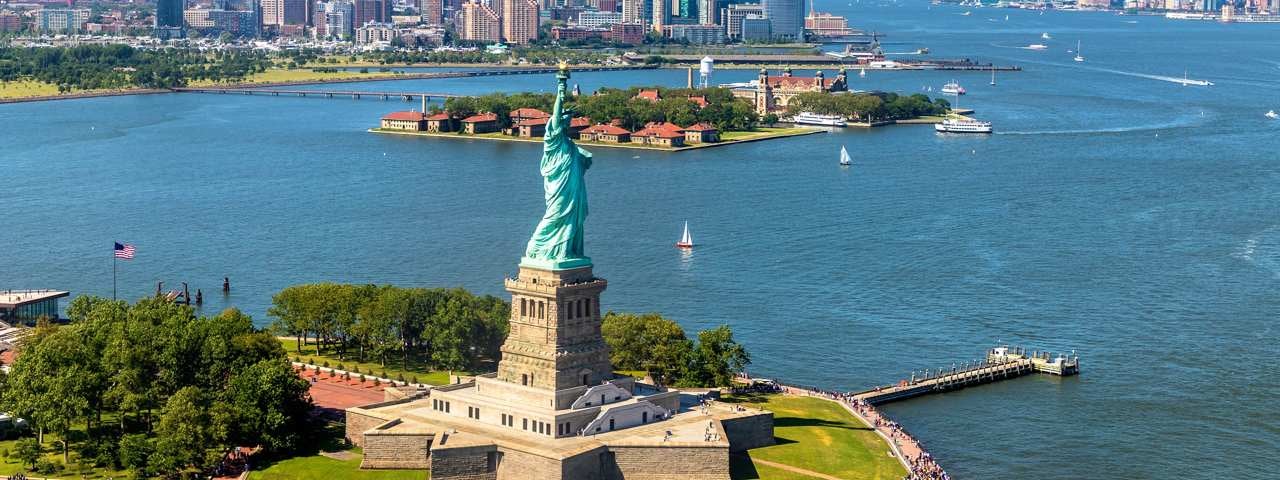 The Statue of Liberty on a sunny and calm day with sail boats on the water surrounding it