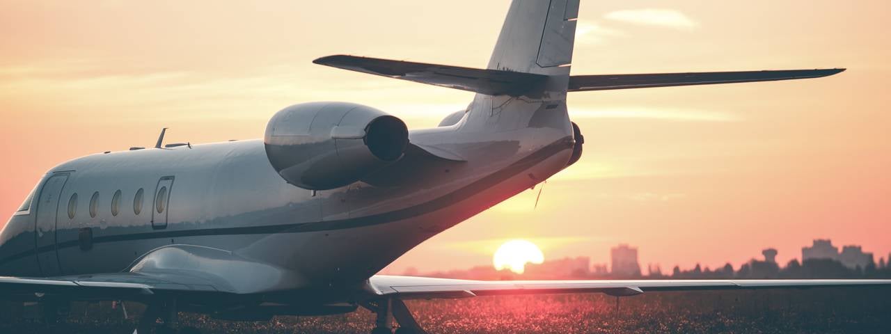 A private jet parked on a runway as the sun sets over a city in the background.