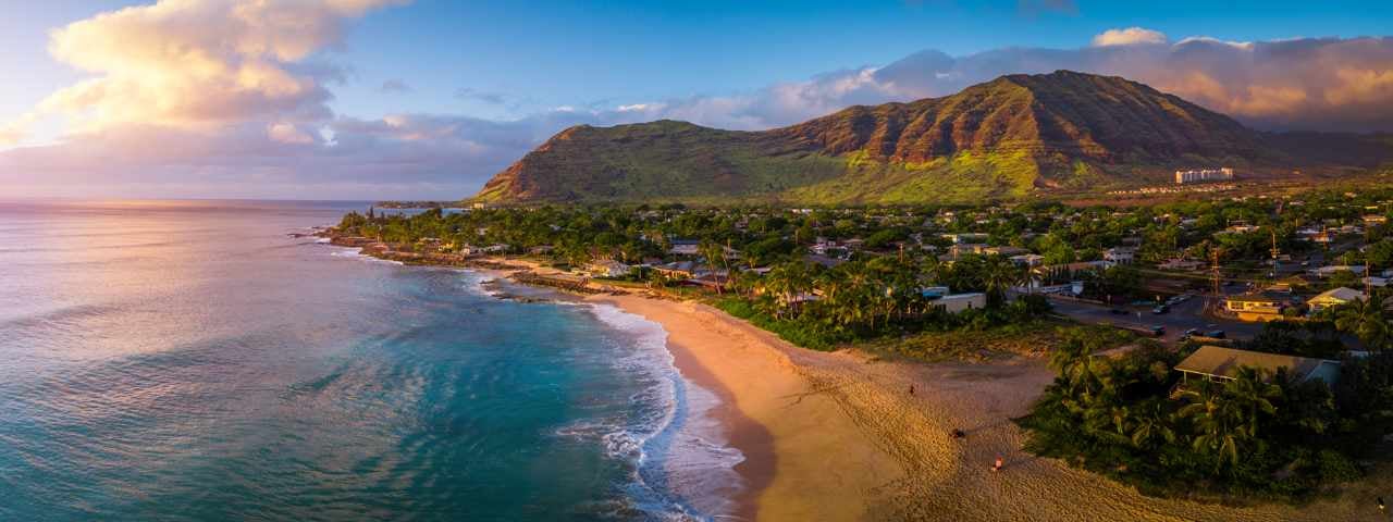 Sunset on the beach and ocean with a mountain in the distance on the island of Oahu in Hawaii.