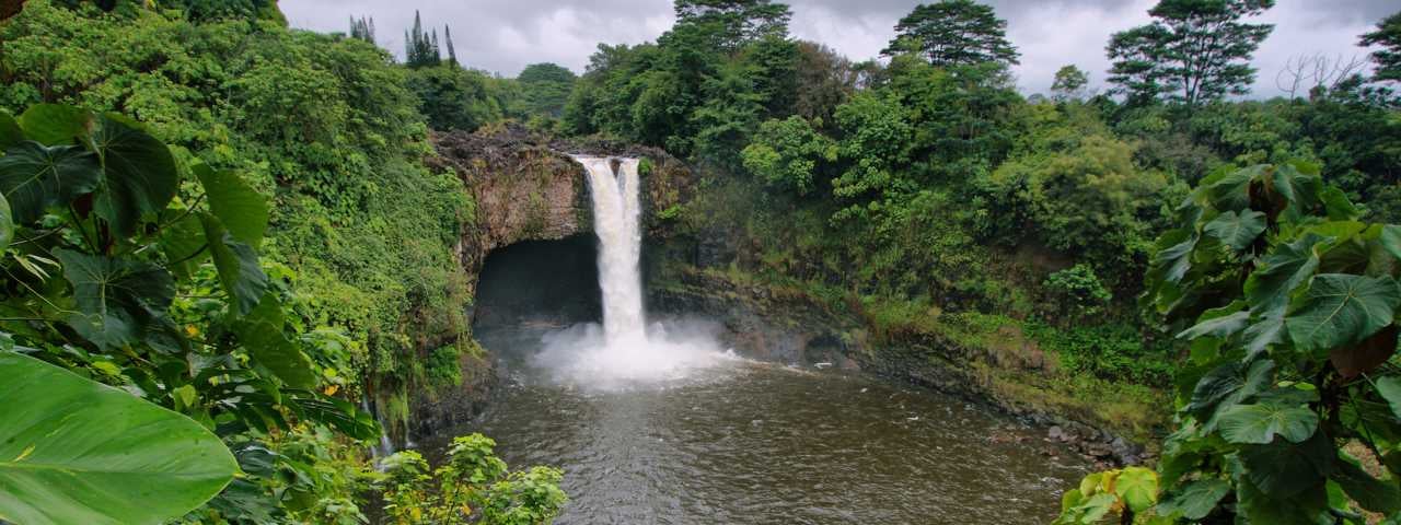Rainbow Waterfalls surrounded by forest on Big Island in Hawaii.
