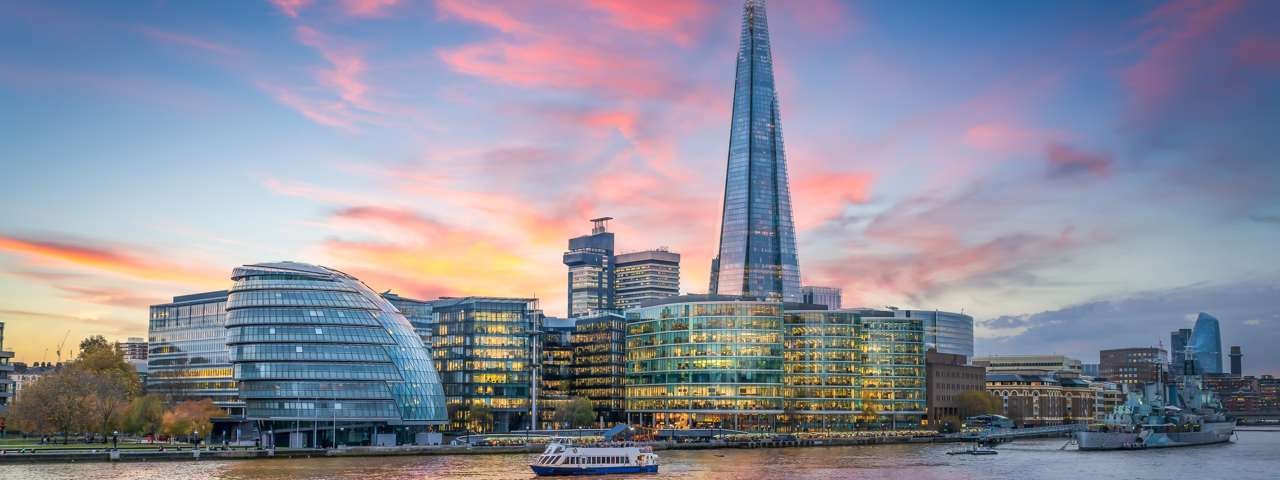 London’s skyline at sunset, with a boat gliding along the River Thames.