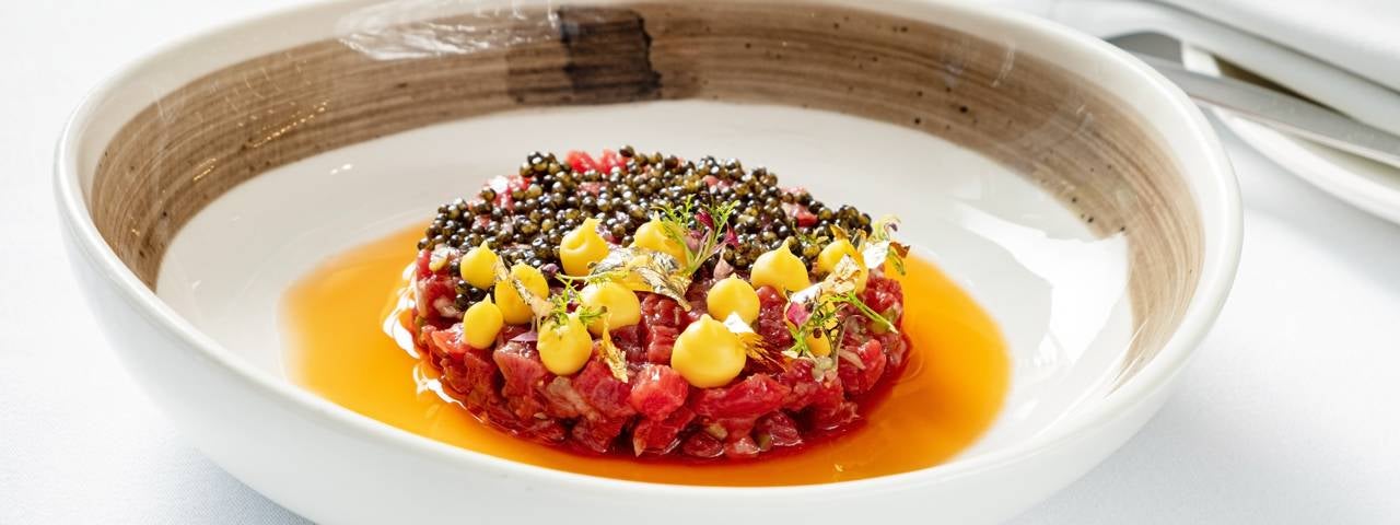 Beef tartare served in a white bowl with a brown inner rim. 