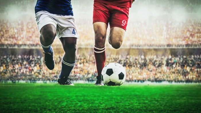 A football player with the ball at his feet in front of a crowd.