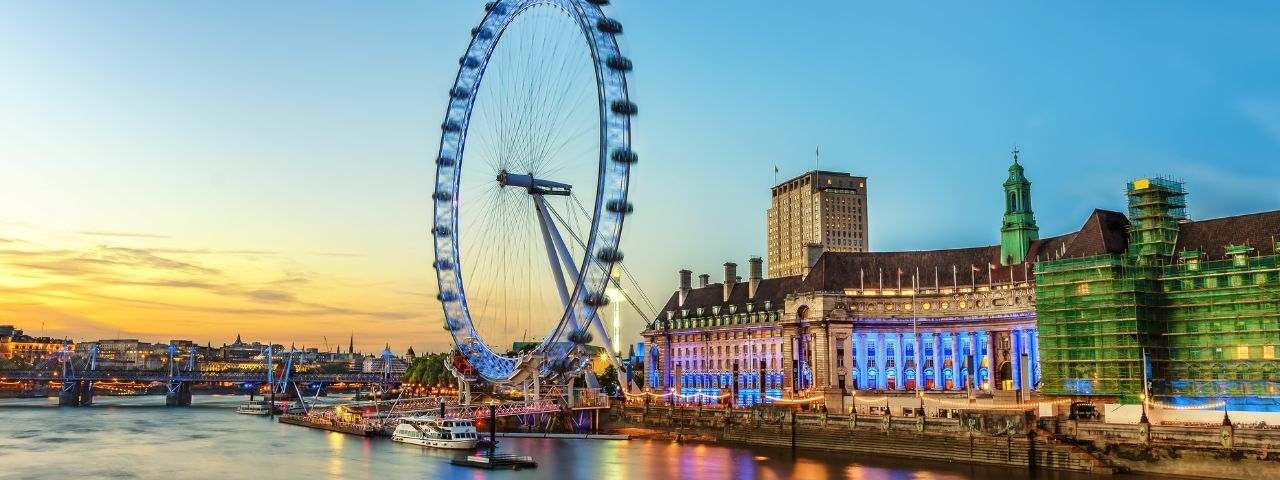 The London Eye and buildings lit by neon lights on the South Bank of the River Thames at night in London, England.
