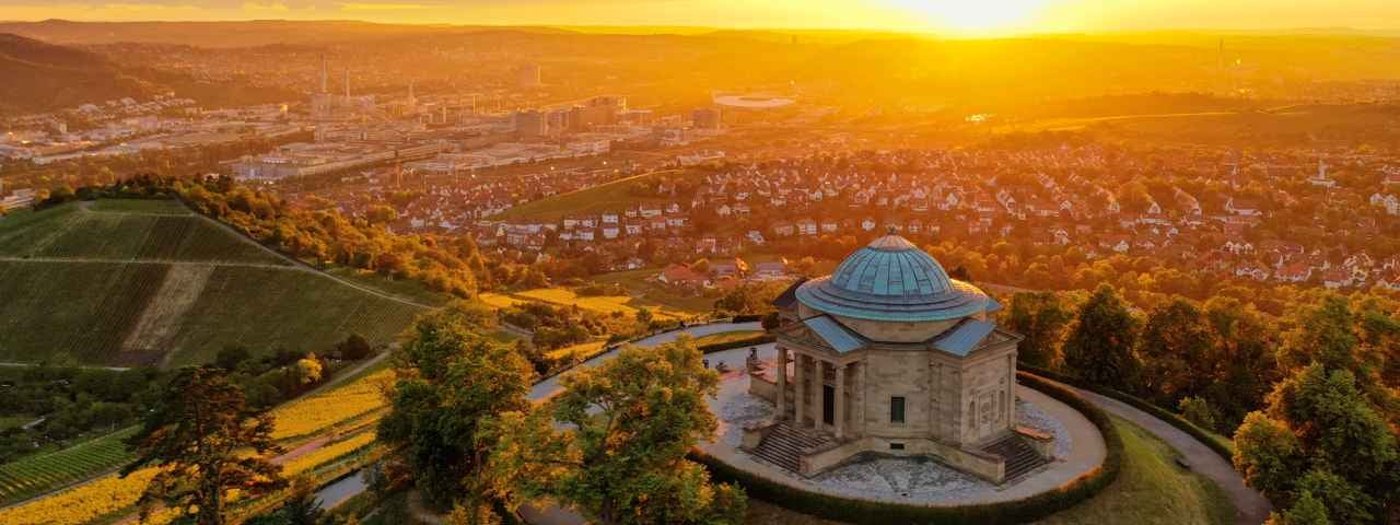 An aerial view of Stuttgart and the Neckar Valley at sunset with an old building on a hill in the foreground.