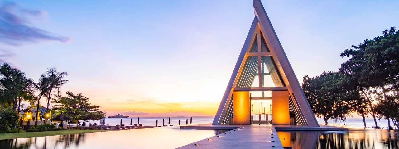 A luxury hotel cabana in a swimming pool with the ocean in the background as the sun sets