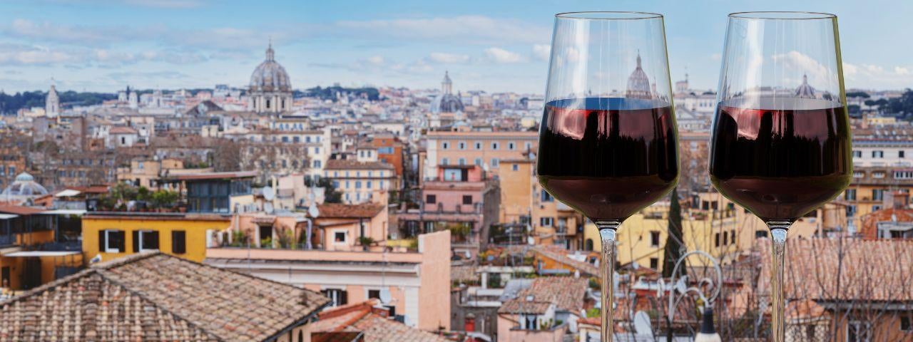 Two glasses of red wine on a table with a view of Rome stretching into the distance.