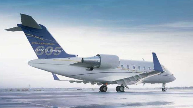 A private jet takes off from a runway with low-hanging clouds in the background.