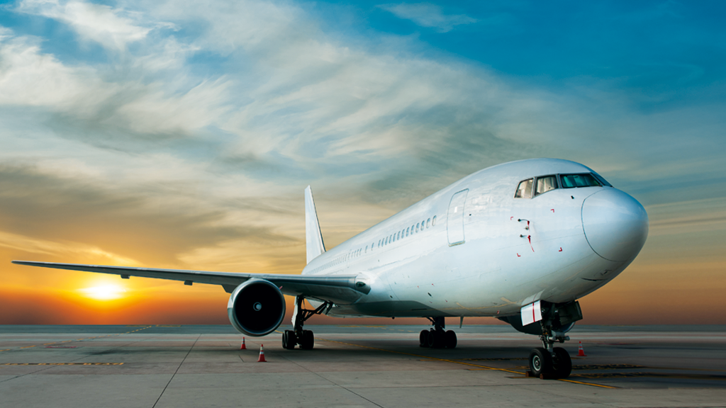 An aeroplane parked on the runway at sunrise.