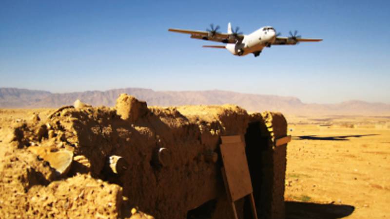 A large aircraft flying over a remote desert.