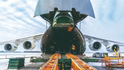The front of a cargo aircraft is open and about to be loaded with cargo.