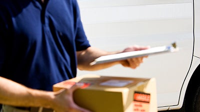 An onboard courier carrying a box and looking at a clipboard.