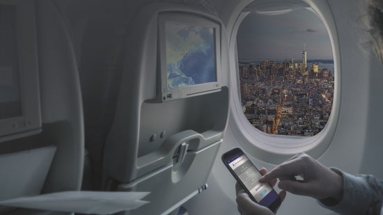 A person looking at their phone on a plane with a city view out of the window.