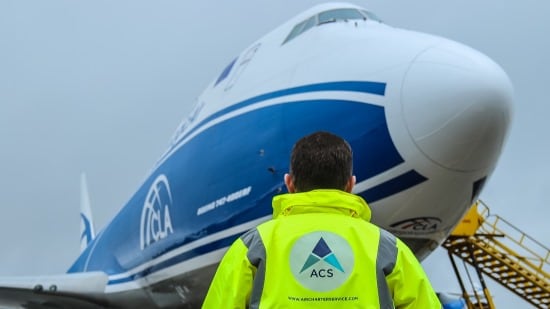 An ACS employee wearing a neon-yellow branded jacket looks up at a plane.