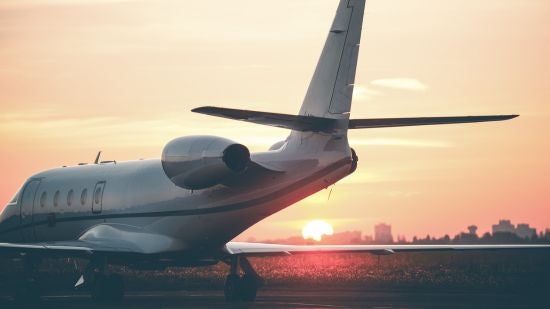 A private jet parked on a runway as the sun sets over a city in the background.