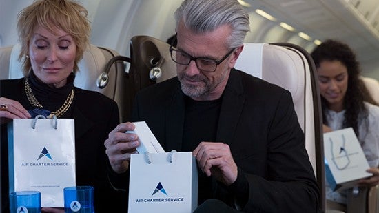  A man and woman on a plane looking at Air Charter Service gift bags.